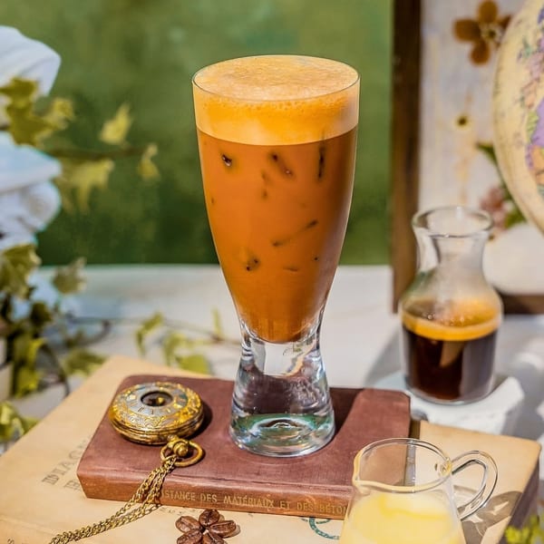 Iced coffee with foam, a pocket watch, coffee beans, and a small pitcher of cream.