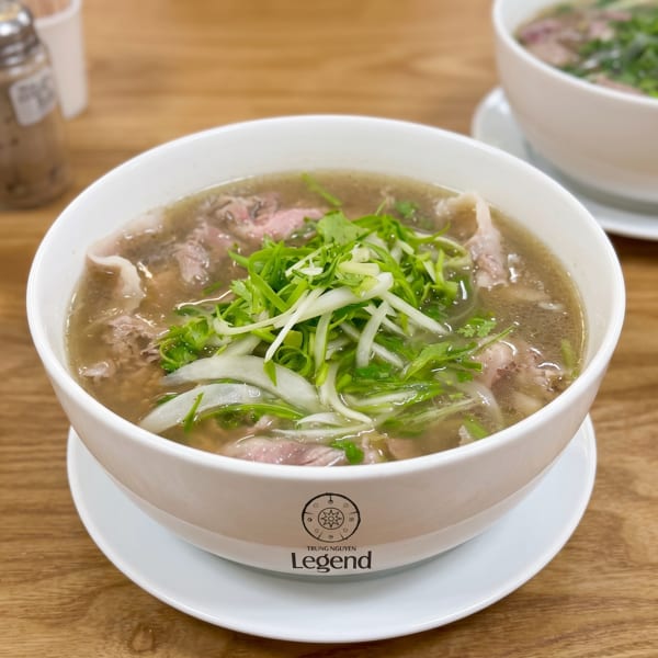 A bowl of Vietnamese pho with beef, green onions, and cilantro on a wooden table.