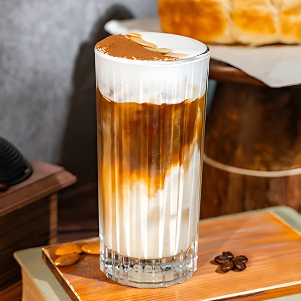 Iced coffee with foamed milk, cocoa powder, and almond slivers, next to coffee beans.